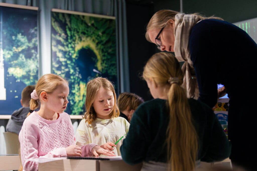 Lapset tekevät koulutehtäviä opettajan kanssa.