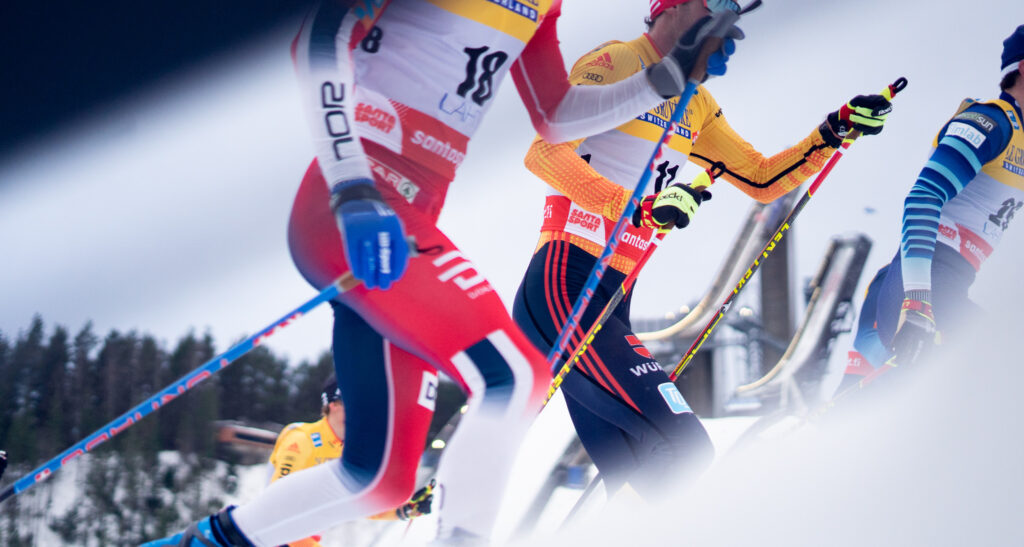 Miehiä hiihtämässä kilpaa Salpausselän kisoissa. Taustalla hyppyrimäet.