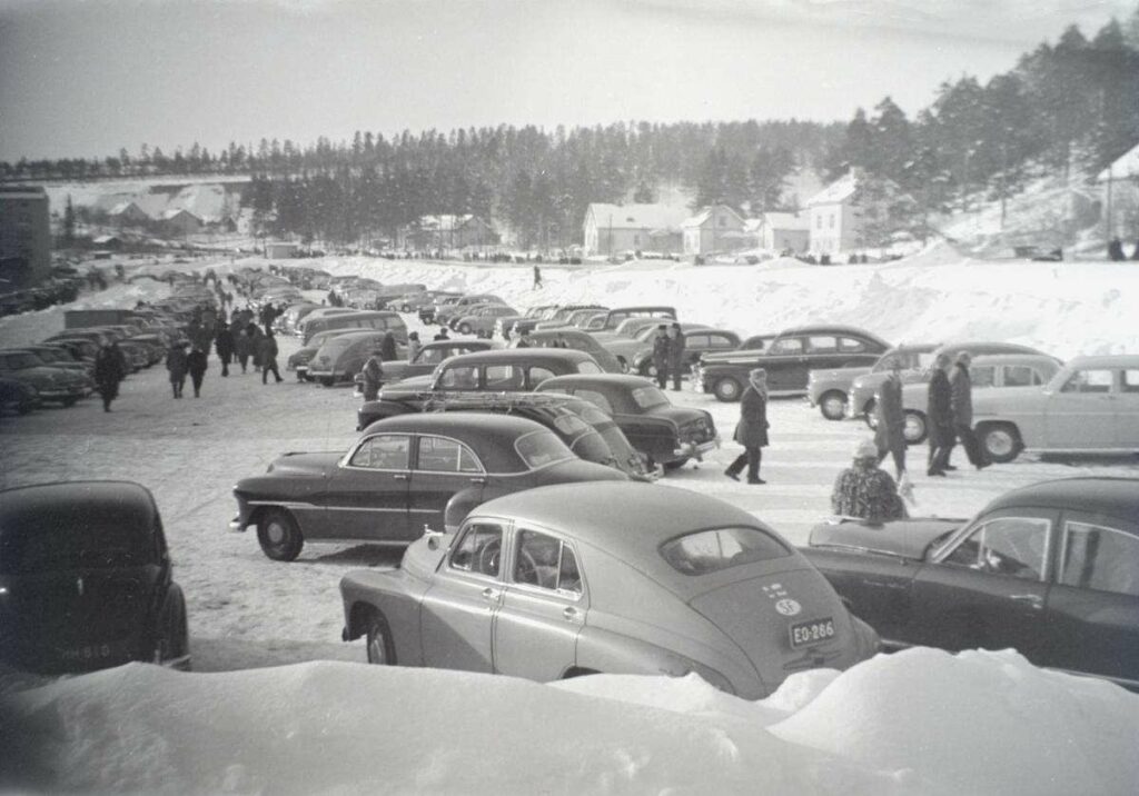 vanhoja autoja parkissa talvisessa maisemassa.